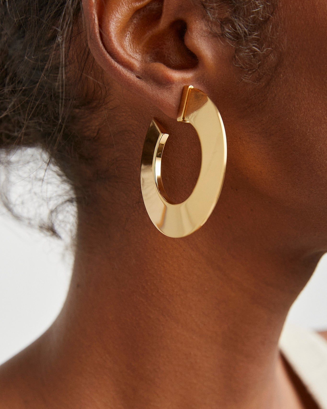 Gold hoop earring worn by a person with a neutral background