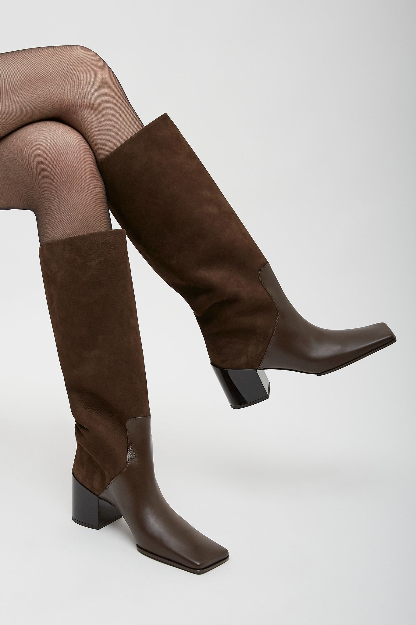 Brown knee-high boots worn with tights on a white background
