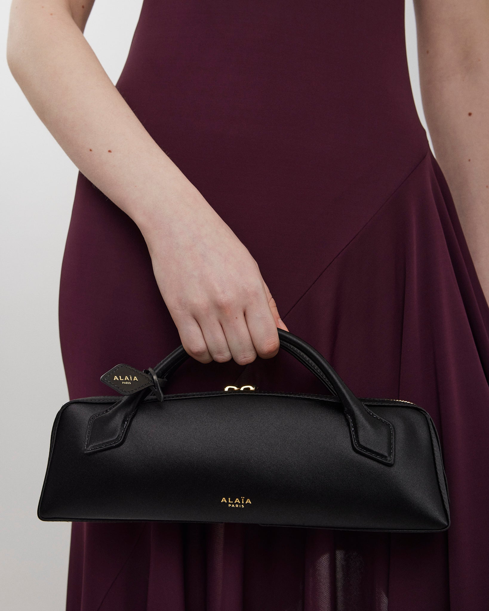 Person holding a black handbag with Alaia branding against a plain background