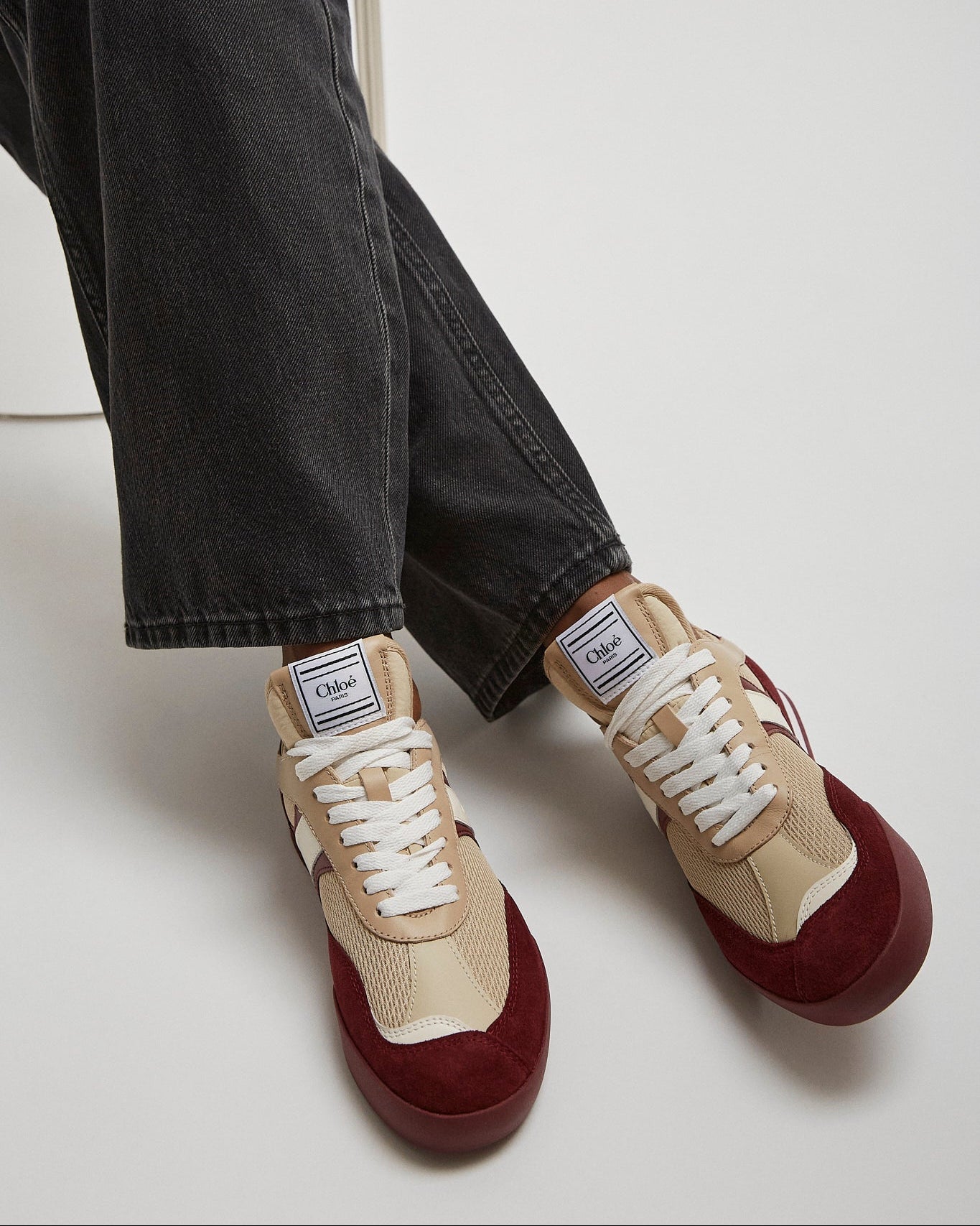 Beige and burgundy sneakers worn with black jeans on a white background