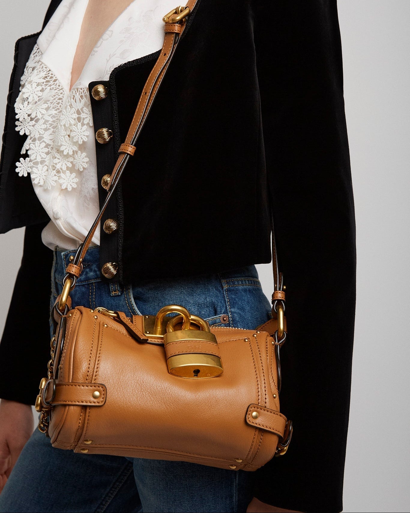Brown leather handbag with gold accents worn by a person against a neutral background