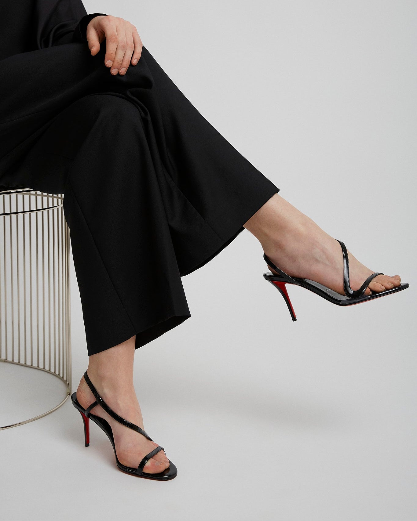 Person wearing black high-heeled sandals with a red sole on a light gray background