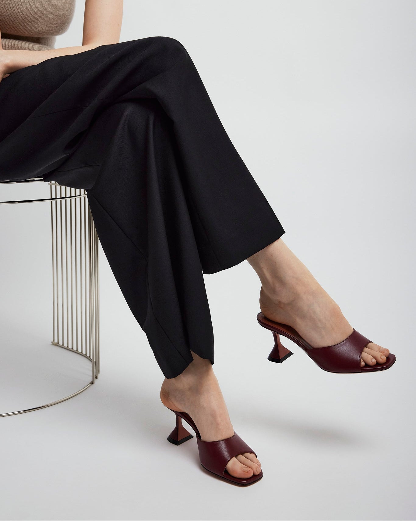Person wearing black pants and brown high-heeled shoes sitting on a metal stool.