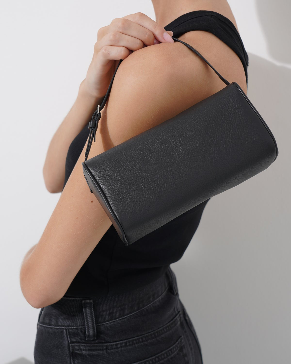 Person holding a black clutch bag against a plain background
