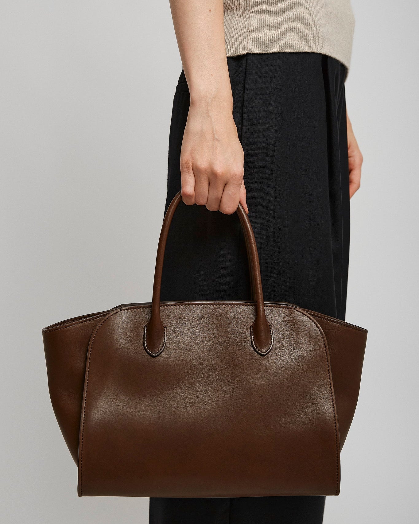 Brown leather handbag held by a person against a plain background