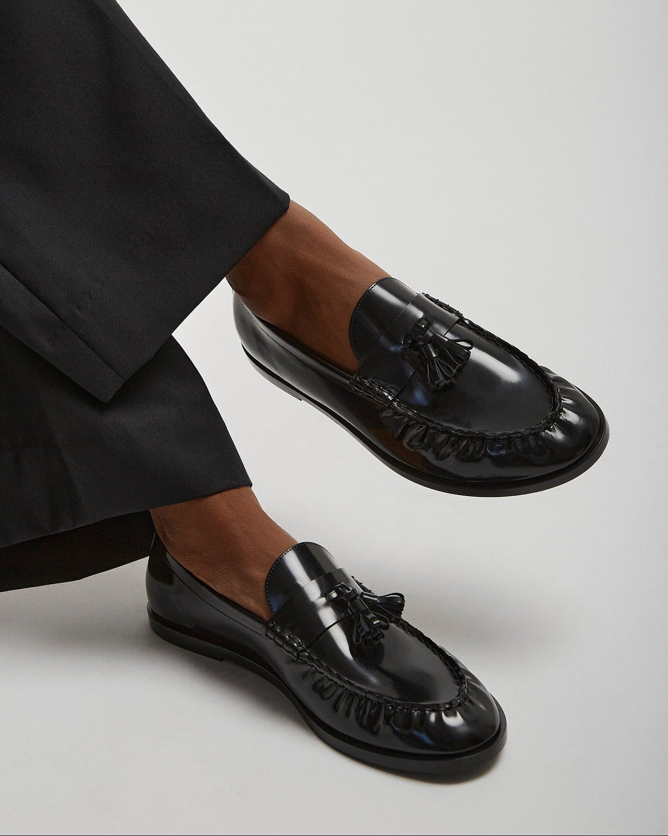 Black loafers worn with black pants on a light gray background