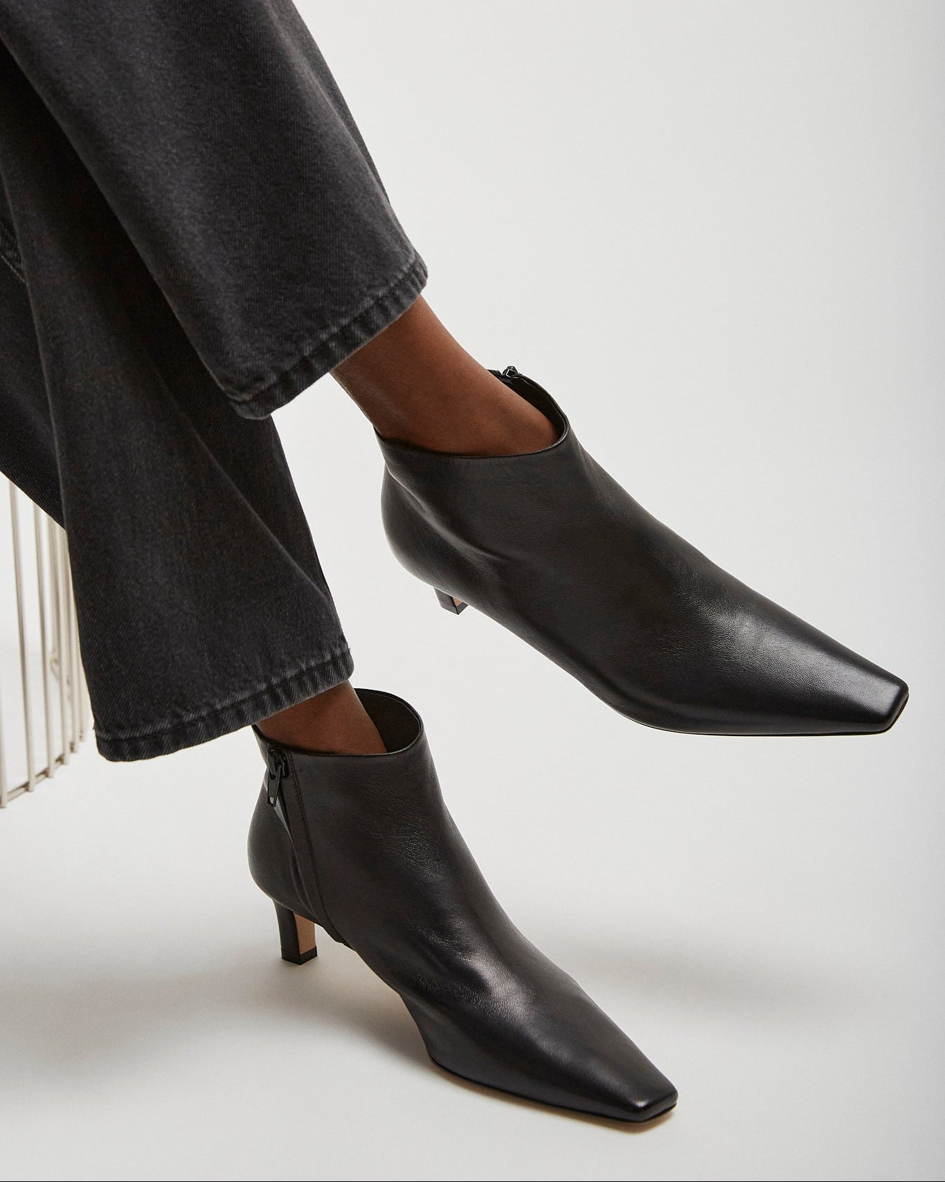 Black ankle boots worn with dark jeans on a light gray background