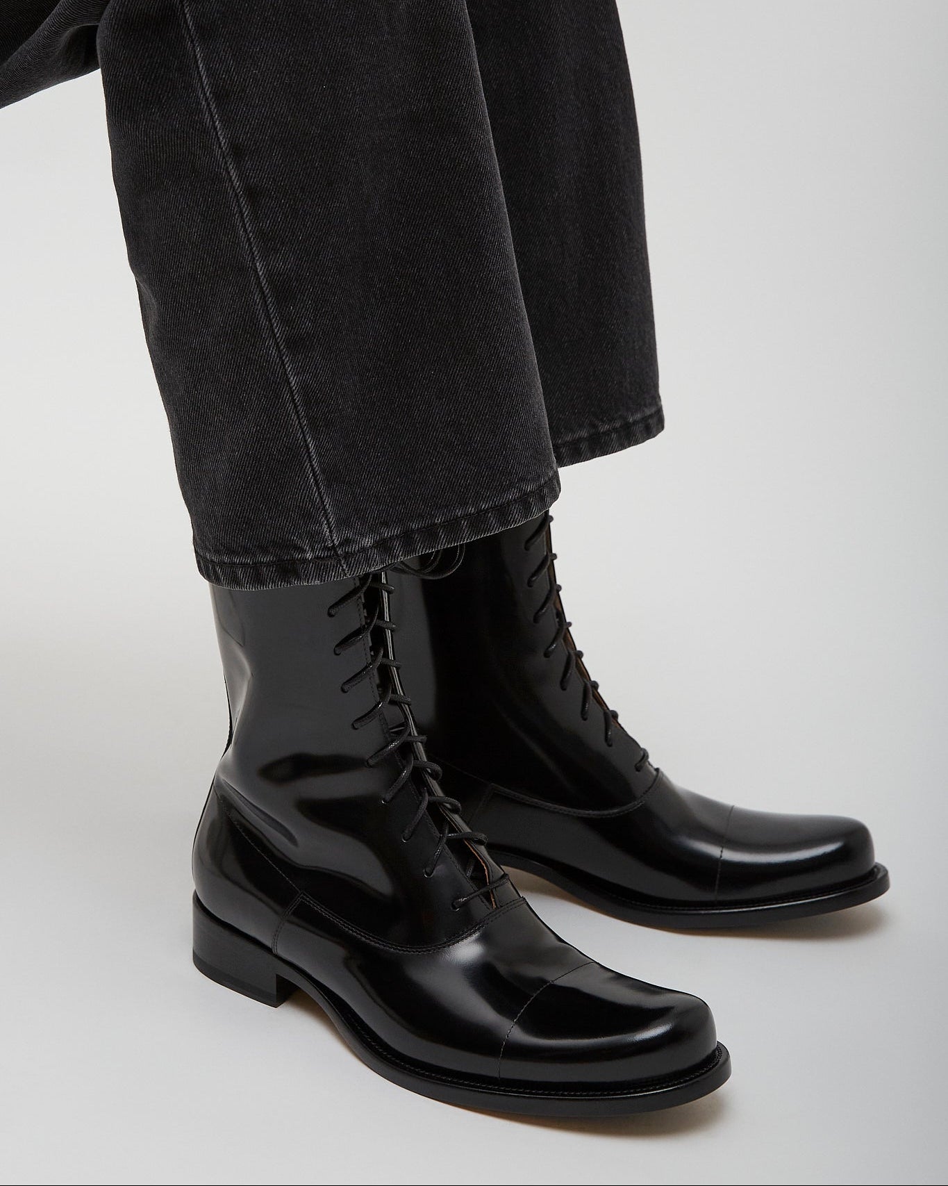 Black leather boots worn with black pants on a light gray background