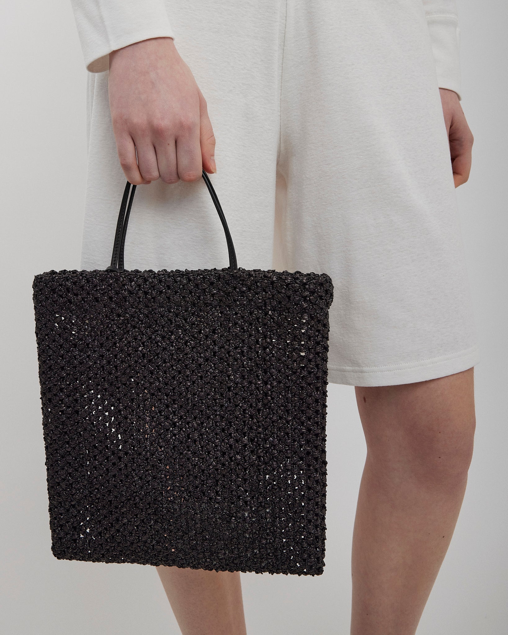 Person holding a black woven handbag against a plain background