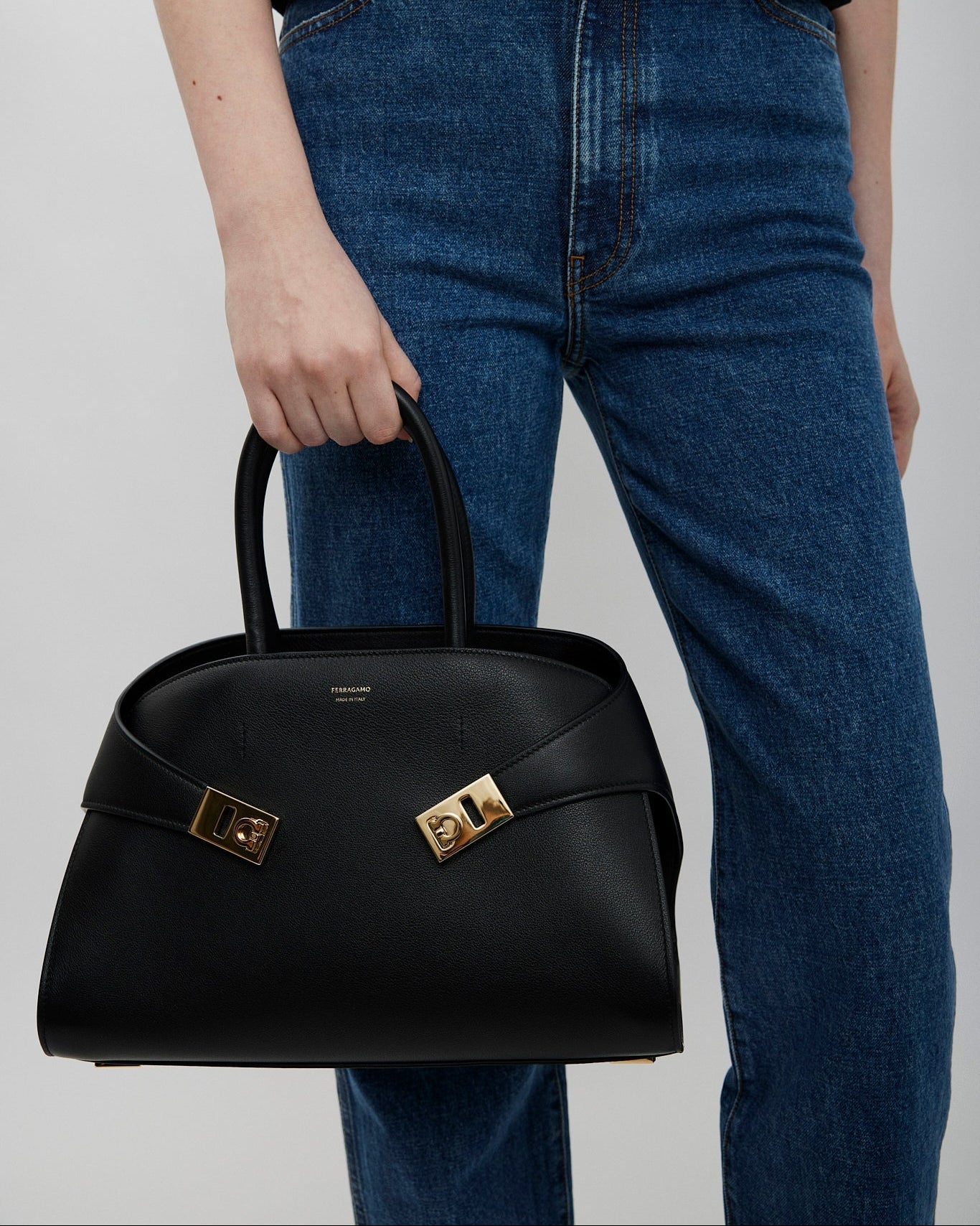 Person holding a black handbag with a gold clasp against a plain background