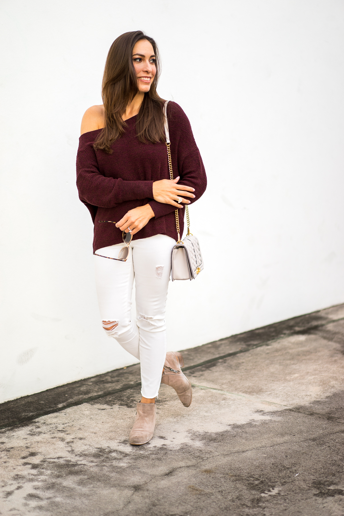 Best Luxury Designers Handbags blogger Amanda Mercado wearing Free People burgundy off the shoulder sweater with white distressed denim and ankle booties