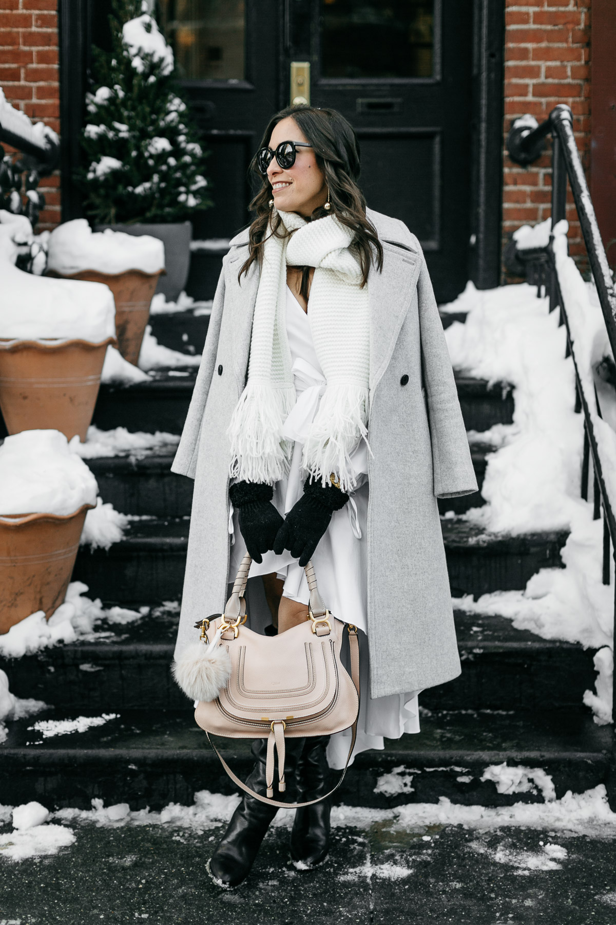 Best Luxury Designers Handbags bloggers wears Carolina Constas high low white shirt dress for NYFW street style while carrying her Chloe Marcie bag and Club Monaco coat and white fringed scarf in Greenwich Village