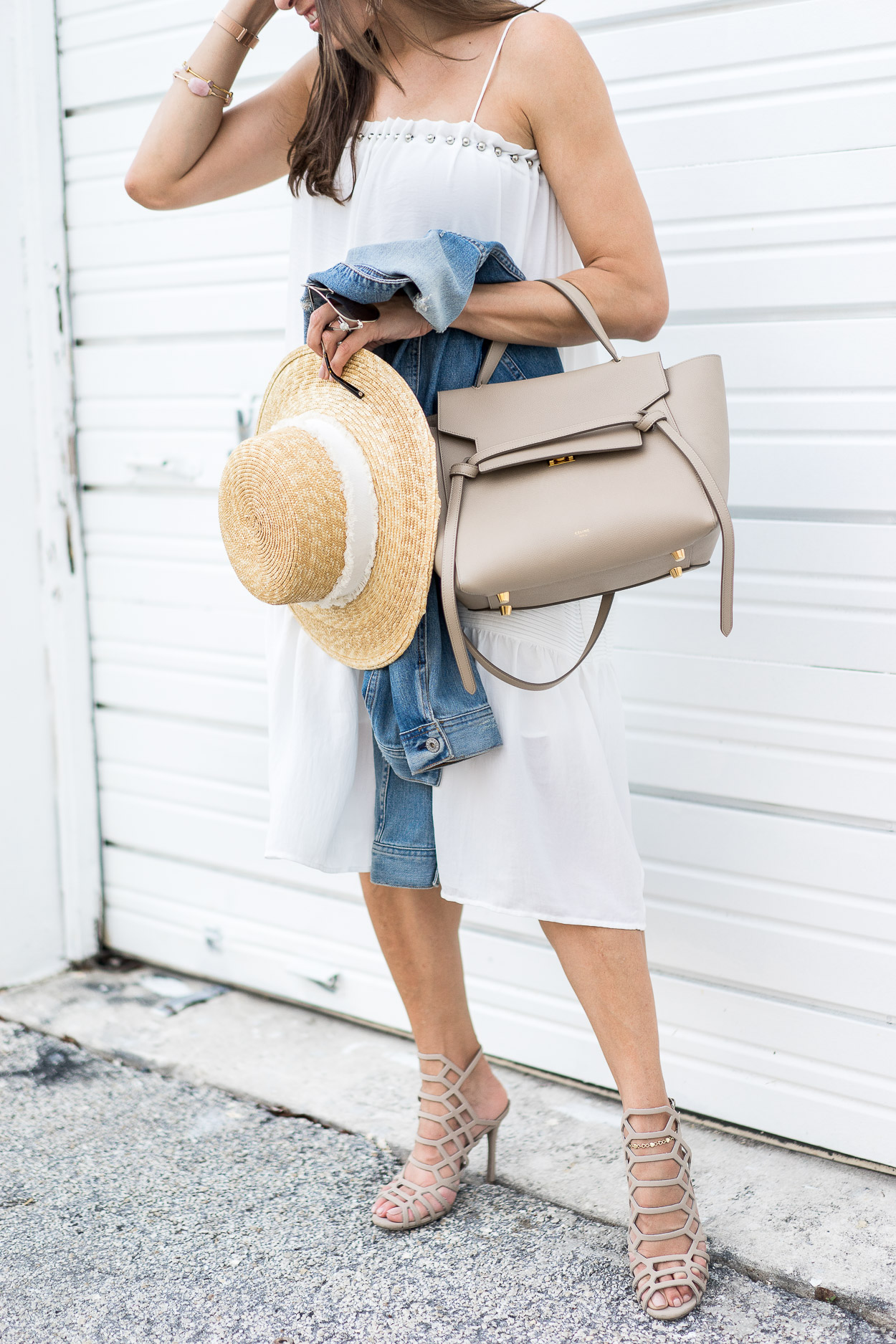  Best Luxury Designers Handbags blogger wearing white dress, holding a straw hat, denim jacket, and a bag 